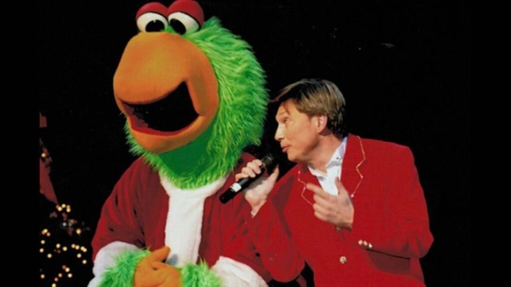 Mark Milovats in red suit with a green character